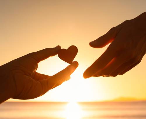 Hand giving heart to another on sunset background